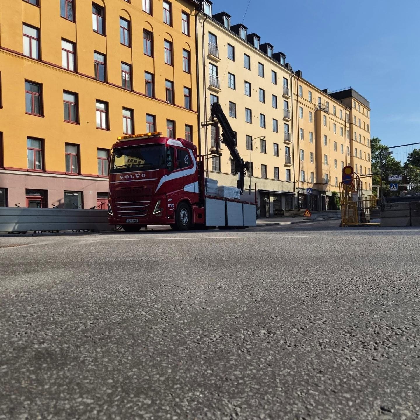 Kranbil som lossar framför gula stenhus