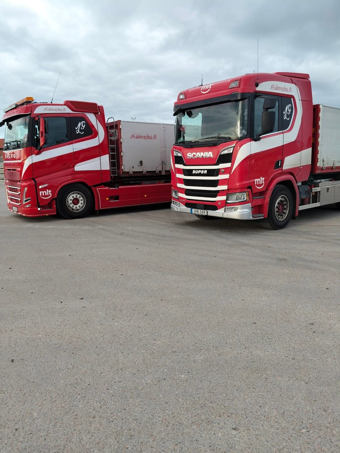 Två röda Scania med flak och kran uppställda bredvid varandra