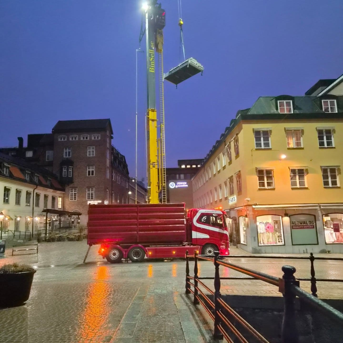 Kvällslyft i en stadsmiljö, lasten hänger i luften framför upplysta fönster